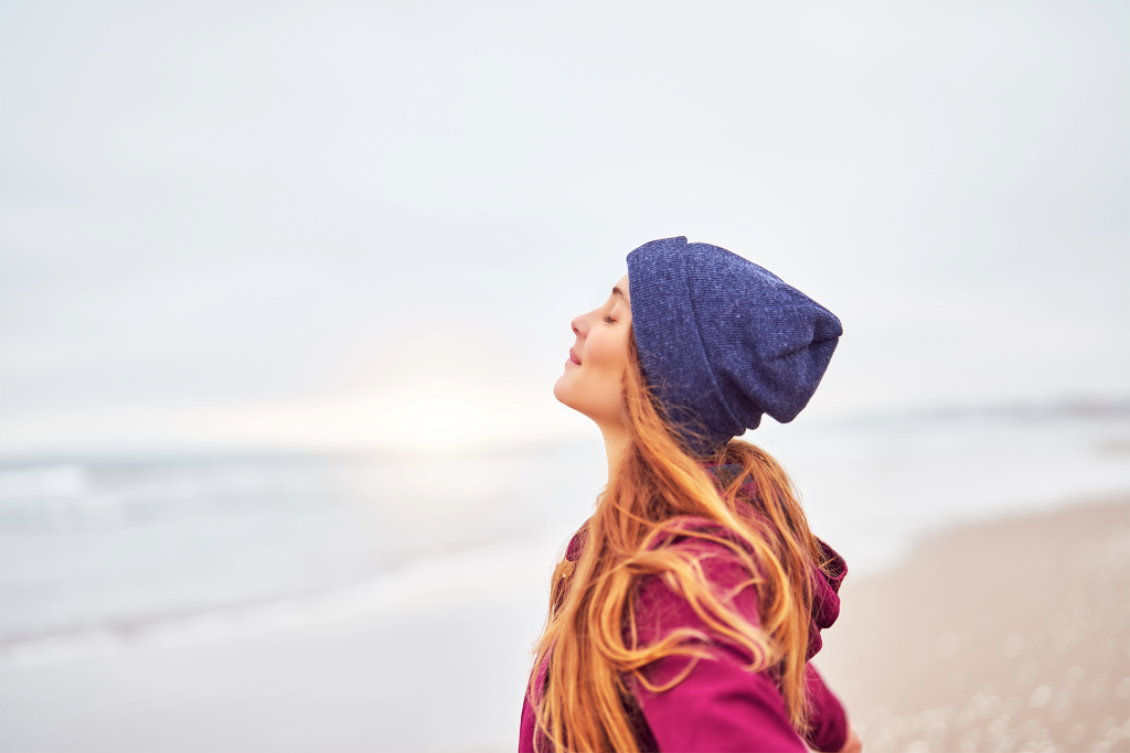 Woman facing the ocean in a stocking hat on the beach